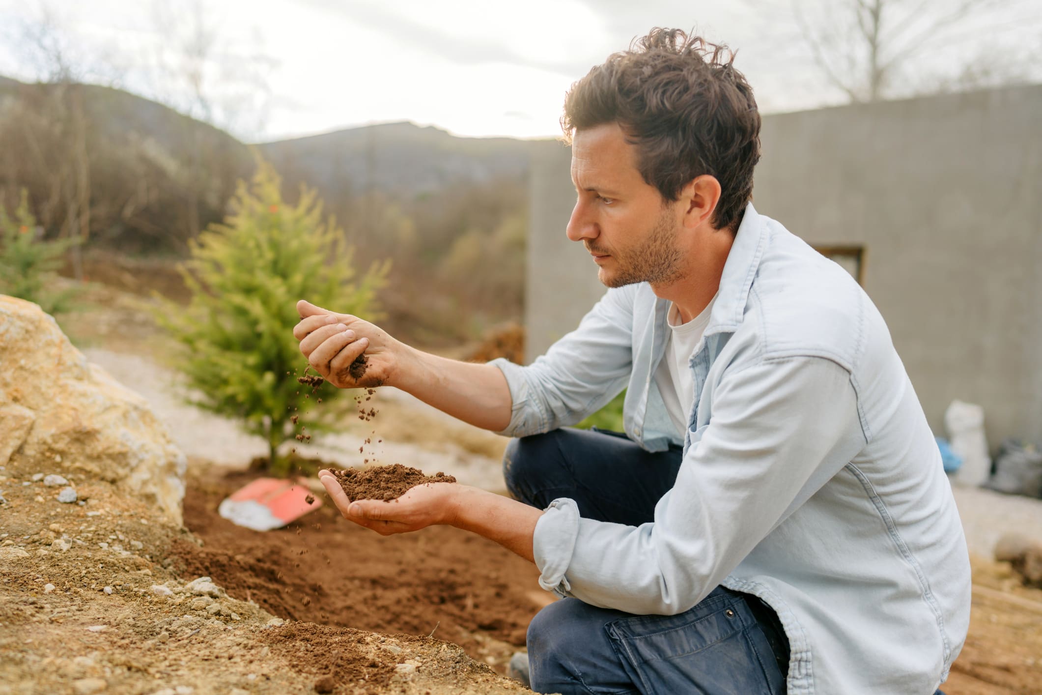 Man examining soil outdoors near house.